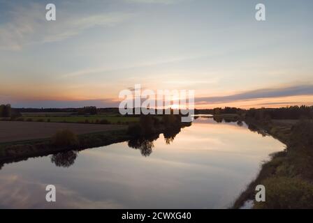 Die Herbstsonne untergeht über den Feldern und dem Fluss in Nordfinnland. Das Flusswasser ist an diesem ruhigen Abend sehr still. Stockfoto