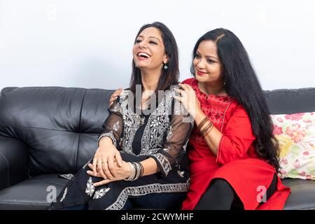 Zwei lächelnde Freundinnen sitzen zu Hause auf einer Couch und haben eine gute Zeit, lachen glücklich aus. Stockfoto
