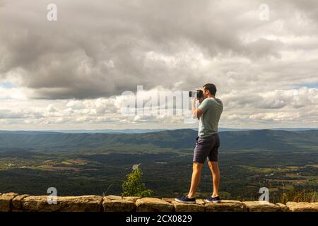 Ein junger kaukasischer Landschaftsfotograf in Kurzform und T-Shirt Macht oben ein Foto vom Shenandoah Valley Von einer Steinbarriere Wand durch einen clif Stockfoto