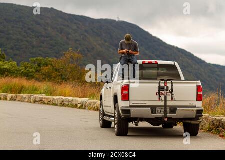 Shenandoah Valley, VA, USA, 09/27/2020: Ein Mann sitzt im Kofferraum eines weißen GMC sierra Pickup LKW auf der Fahrerkabine und spielt mit seinem Telefon. Stockfoto