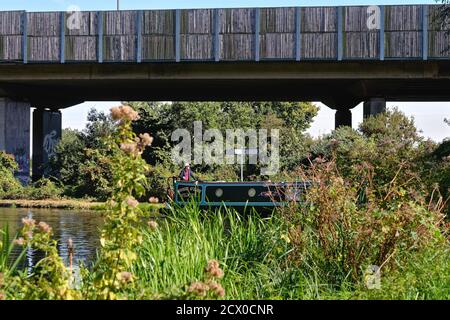 Ein Kanal schmales Boot unter der Autobahn M25 vorbei Der River Wey Navigation Kanal in New Haw Surrey England VEREINIGTES KÖNIGREICH Stockfoto