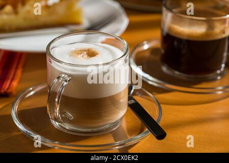 Zwei Tassen Kaffee und Cappuccino mit Kuchen auf Holztisch. Stockfoto