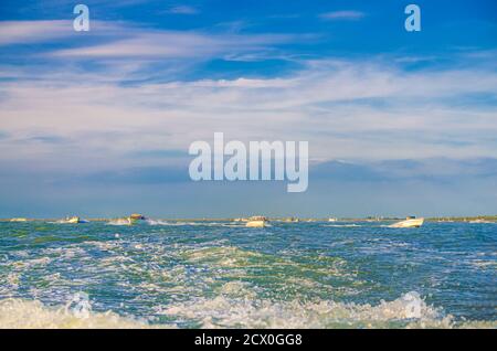 Segelboote, die auf dem Wasser der venezianischen Lagune zwischen Holzmasten in der Nähe der Stadtküste von Venedig, Insel am Horizont, Region Venetien, Norditalien segeln Stockfoto