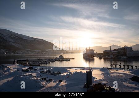 Tromsø Hafen mit Kreuzfahrtschiff und Sonnenuntergang hinter dem Berg im Winter. Panoramablick. Stockfoto