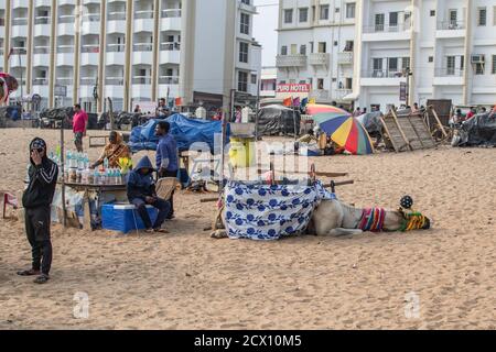 Puri, Indien - 3. Februar 2020: Ein dekoriertes Kamel ruht am Strand mit nicht identifizierten Menschen in der Nähe, die Wasser am 3. Februar 2020 in Puri, Indi verkauft Stockfoto