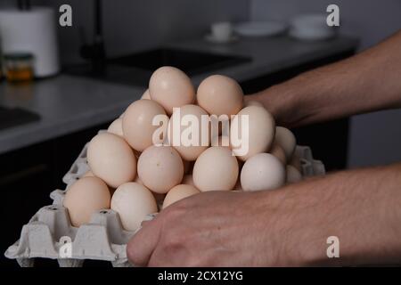 Männliche Hände halten ein Fach, das nach oben mit gefüllt ist Hühnereier Stockfoto