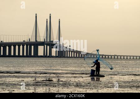 George Town, Penang/Malaysia - Dez 28 2019: Fischer werfen Netz. Hintergrund ist Penang Second Bridge. Stockfoto