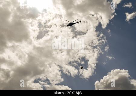 Hintergrundbeleuchtete Ansicht der Silhouette eines Hubschraubers, der Ladung gegen bewölkten Himmel trägt, Courmayeur, Aostatal, Italien Stockfoto