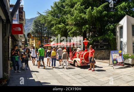 Ein roter, kleiner Zug in der Hauptfußgängerzone der berühmten Bergstadt geparkt, die im Sommer von Touristen überfüllt ist, Courmayeur, Aosta, Italien Stockfoto