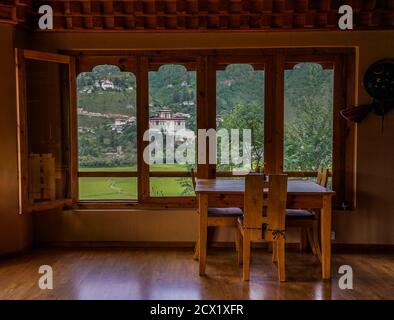 Blick durch ein Fenster auf Rinpung Dzong (Paro Dzong), buddhistisches Kloster und Festung und Reisfelder im Paro-Tal, Bhutan Stockfoto