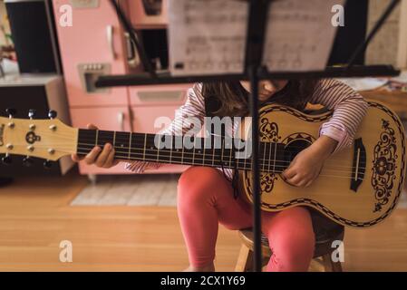 Junges Mädchen auf Hocker sitzen Kommissionierung die Fäden von klein Verzierte Gitarre Stockfoto