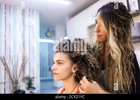 Friseur Kämmen Client mit langen lockigen Haar gegen den Wandspiegel Im Friseursalon Stockfoto