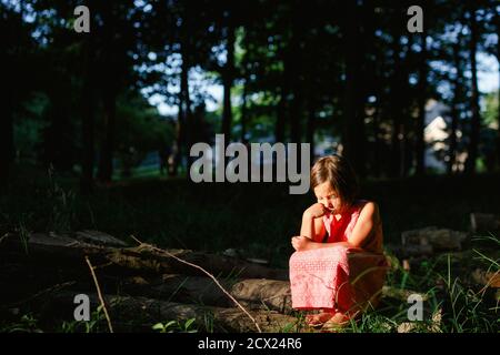 Ein kleines unlorn Kind sitzt im Sonnenlicht in einem schattigen Waldstück Stockfoto