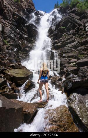 Rückansicht einer Frau, die auf einem Felsen bei einem Wasserfall steht Stockfoto