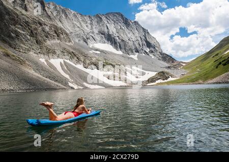 Frau, die sich auf dem Floß am Pool im See gegen den Berg erholte Stockfoto