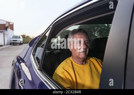 Ein alter Mann, der auf dem Rücksitz eines sitzt Elektroauto bei geöffnetem Fenster Stockfoto