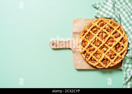 Oben mit einem frisch gebackenen Apfelkuchen auf einem grünen Tisch, selbstgebackenen Apfelkuchen mit Gitterkruste auf einem Holzbrett. Stockfoto