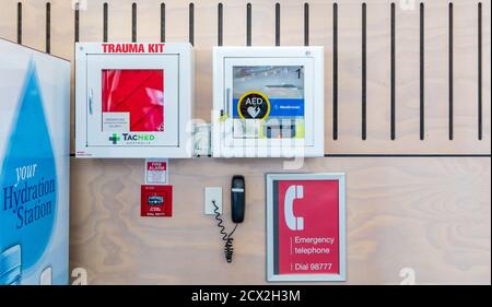 Ein Trauma-Kit, Defibrillator (AED), Feueralarm-Taste und Notrufnummer, wandmontiert im Passagierterminal des Auckland International Airport, NZ Stockfoto