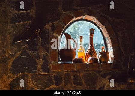 Alte rustikale Weinflaschen, Krüge auf einem kleinen Kellerfenster an einer Steinmauer Stockfoto