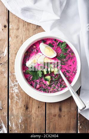 Kalte Rote Beete Suppe mit Gurke, Ei und Kräutern auf einem Holztisch. Stockfoto