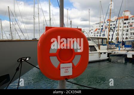 Nur für den Notfall. Eine leuchtend orange Lifebuoy und Gehäuse auf einem Pfosten mit einem Marina Hintergrund platziert. Stockfoto