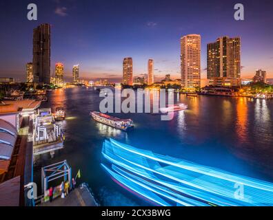 Wolkenkratzer und leichte Verkehrswege auf dem Chao Phraya Fluss in Bangkok, Thailand, von der Taksin Brücke bei Nacht gesehen
