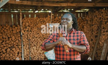 Afrikanischer Mann mit der Axt, die für den Winter vor dem Holzstapel steht. Hochwertige Fotos Stockfoto