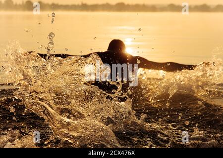 Starker Mann in Silhouette Schwimmen am See im Schmetterlingsstil Stockfoto