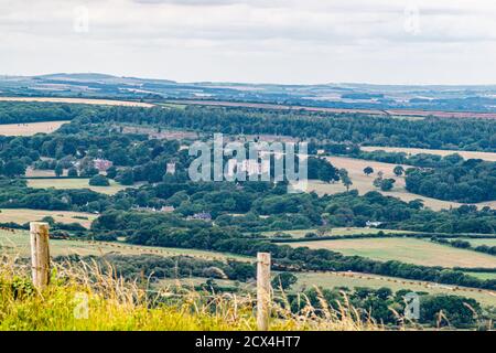 Fernsicht auf Schloss Lulworth in Wareham, große Felder am Meer mit altem Schloss umgeben von Wäldern und Hügeln, bedecktem Himmel und gut Stockfoto