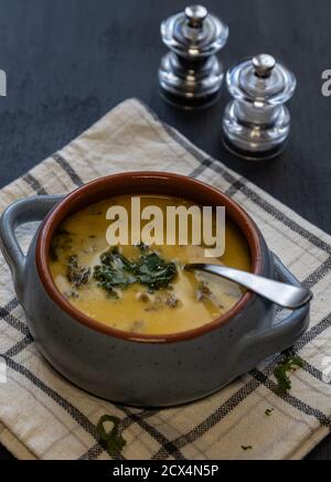 High-Angle-Schuss einer Kartoffel, Wurst und Grünkohl-Suppe in einer blauen und orangen Schüssel auf einem Geschirrtuch vor einem dunkelblauen Hintergrund. Stockfoto