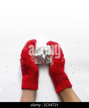 Hände in gestrickten Fäustlingen mit Geschenkbox auf weißem Tisch. Stockfoto