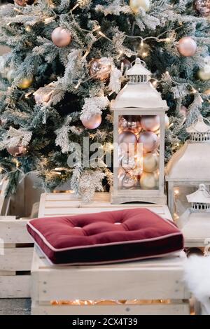 Laterne mit Weihnachtskugeln auf geschmücktem christbaumhintergrund im Wohnzimmer. Winterzeit und Lampe auf Holzsofa in der Nähe von weihnachtsbaum. Stockfoto