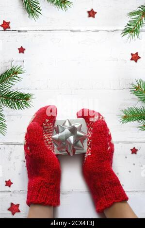 Hände in gestrickten Fäustlingen mit Geschenkbox auf weißem Holztisch. Stockfoto