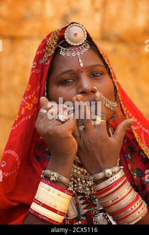Portrait einer Rajasthani Frau in unverwechselbaren Rajasthani Kleid und Schmuck spielen eine Maultrommel, Jaisalmer, Indien. Dieses Bild enthält kulturell relevantes Material: 1. Rajasthani ethnischen Schmuck. 2. Ein Sari ist ein südasiatisches Frauenkleid, das aus einem Tuch mit einer Länge von 4 bis 8 Metern und einer Breite von 60 bis 1,20 Metern besteht, das normalerweise um die Taille gewickelt ist, wobei ein Ende über die Schulter drapiert ist und das Mittelriff entblößte. Der Sari wird normalerweise über einem Petticoat getragen. Der Sari ist mit Gnade verbunden und gilt weithin als Symbol der indischen Kultur. Stockfoto