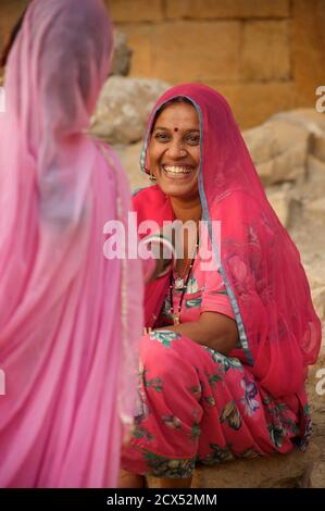 Rajasthani Frauen, die Wasser von einem Brunnen an Amar Sagar, Lodurva, nr Jaisalmer, Rajasthan, Indien tragen. Ein Sari ist ein südasiatisches Frauenkleid, das aus einem Tuch mit einer Länge von 4 bis 8 Metern und einer Breite von 60 bis 1,20 Metern besteht, das normalerweise um die Taille gewickelt ist, wobei ein Ende über die Schulter drapiert ist und das Mittelriff entblößte. Der Sari wird normalerweise über einem Petticoat getragen. Der Sari ist mit Gnade verbunden und gilt weithin als Symbol der indischen Kultur. Stockfoto