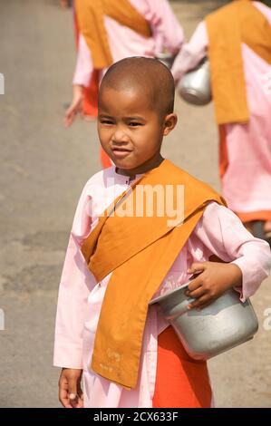 Novize buddhistische Nonne sammeln Almosen, Hsipaw, Burma. Myanmar die traditionelle Erscheinung von Theravadan Bhikkhunis ist fast identisch mit der von männlichen Mönchen, einschließlich eines rasierten Kopfes, rasierte Augenbrauen und Safranroben. In einigen Ländern tragen Nonnen dunkle Schokoladenroben oder manchmal die gleiche Farbe wie Mönche. Weiße oder rosa Roben werden von Theravadan Nonnen getragen, die nicht vollständig ordiniert sind. Diese Nonnen sind in Myanmar (Burma) als Silashin bekannt Stockfoto