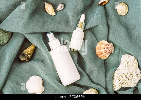 Weiße Kosmetikflaschen auf blauem Textilhintergrund mit Muschelschalen. Naturkosmetik-Konzept, Draufsicht, flach liegend. Stockfoto