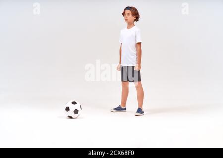 Junger Fußballspieler. In voller Länge Aufnahme eines Teenagers, der auf grauem Hintergrund Fußball spielt, während er wegspielt Stockfoto