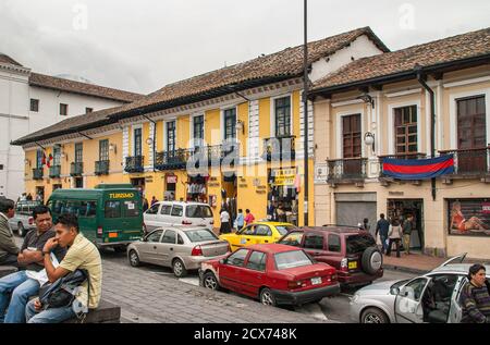Quito, Ecuador - 2. Dezember 2008: Historische Innenstadt. Kleine Einzelhandelsgeschäfte in gelb lackierten alten Gebäuden entlang der Straße mit Autos und Fußgängern. Stockfoto