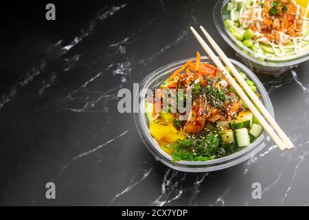 Japanische Gerichte zum Mitnehmen auf schwarzem Marmorboden, Poke, japanische Gewürze, Wakame, Edamame. Stockfoto
