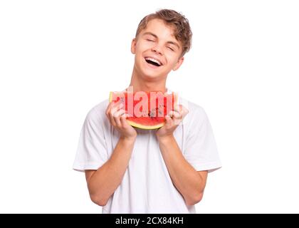 Teen junge Essen reif saftig Wassermelone und lächelnd. Netter Teenager mit Scheibe gesunde Wassermelone. Glückliches Kind trägt weißes T-Shirt, isoliert auf weiß. Stockfoto