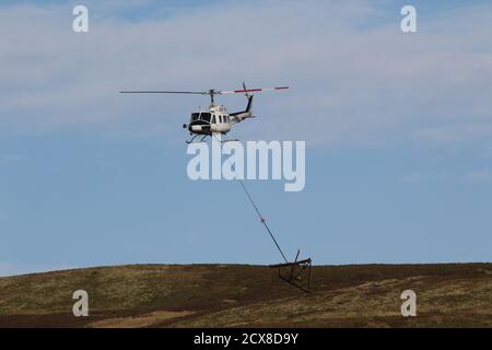 G-UHGB, eine Bell 205A-1, die von Heli-Lift Services betrieben wird, führt Pylonen-Abbauarbeiten in den Hügeln von Renfrewshire/Inverclyde in Schottland durch. Stockfoto