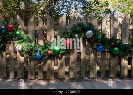 Ein heller strukturierter Holzzaun mit einer Weihnachtsgirlande, die in der Mitte der Barriere entlang geschlungen ist. Stockfoto