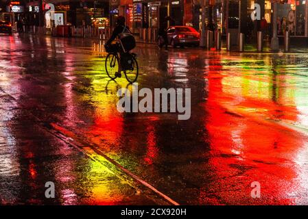 New York, New York, USA. September 2020. Ein Radfahrer fährt durch Regen auf nassen nächtlichen Straßen, die die bunten Lichter am Times Square in New York City reflektieren. Quelle: Stephanie Keith/ZUMA Wire/Alamy Live News Stockfoto