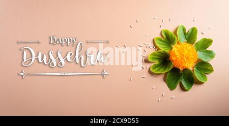 Frohes Dussehra. Gelbe Blüten, grünes Blatt und Reis auf orangefarbenem pastellfarbenem Hintergrund. Dussehra Indian Festival Konzept. Stockfoto