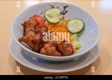 Selektiver Fokus, Torino Karaage, japanisches gebratenes Huhn, servieren mit Salat in weißer Schüssel auf Holztisch. Stockfoto