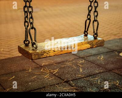 Nahaufnahme einer Schaukel auf Metallketten mit einem Gelber Holzsitz im Abendlicht Stockfoto