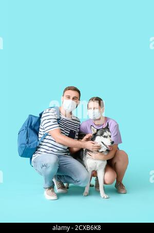 Junges Paar mit medizinischen Masken und niedlichen Husky Hund auf Farbhintergrund. Konzept der Epidemie Stockfoto