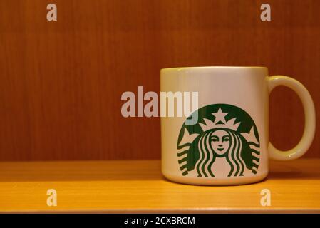Florianopolis, Brasilien. 14. September 2020: Porzellanbecher von Starbucks auf einer Holzbank und gelbliche Beleuchtung. Speicherplatz kopieren. Starbucks ist ein Café Stockfoto