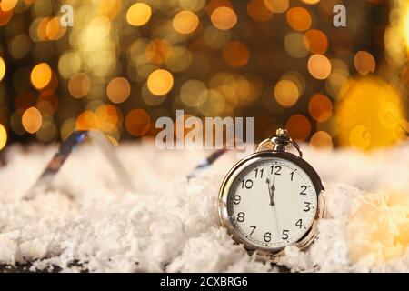 Taschenuhr auf Schnee gegen verschwommenes Licht. Weihnachtszeit Stockfoto